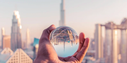 Photo of a hand holding a transparent sphere, with the Dubai skyline behind